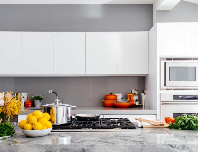 Modern white kitchen with marble countertop, gas stove, orange cookware, and a bowl of lemons in the foreground.